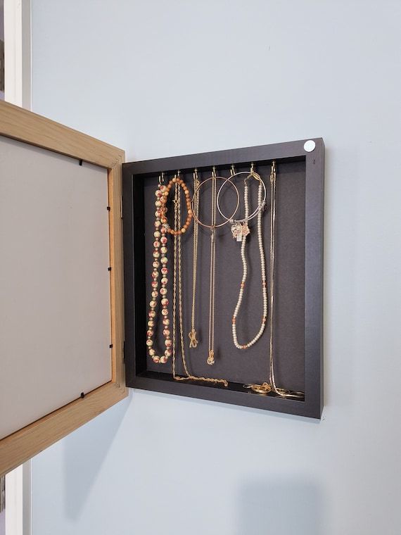 Vägghängt smyckeskrin med halsband och armband prydligt upphängda på krokar.